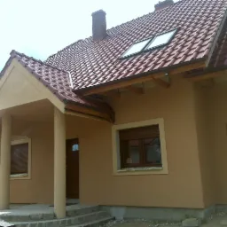 Dom jednorodzinny z nową elewacją w odcieniach beżu i brązu, widoczne okna połaciowe, okna z roletami zewnętrznymi i wejście z kolumnami.