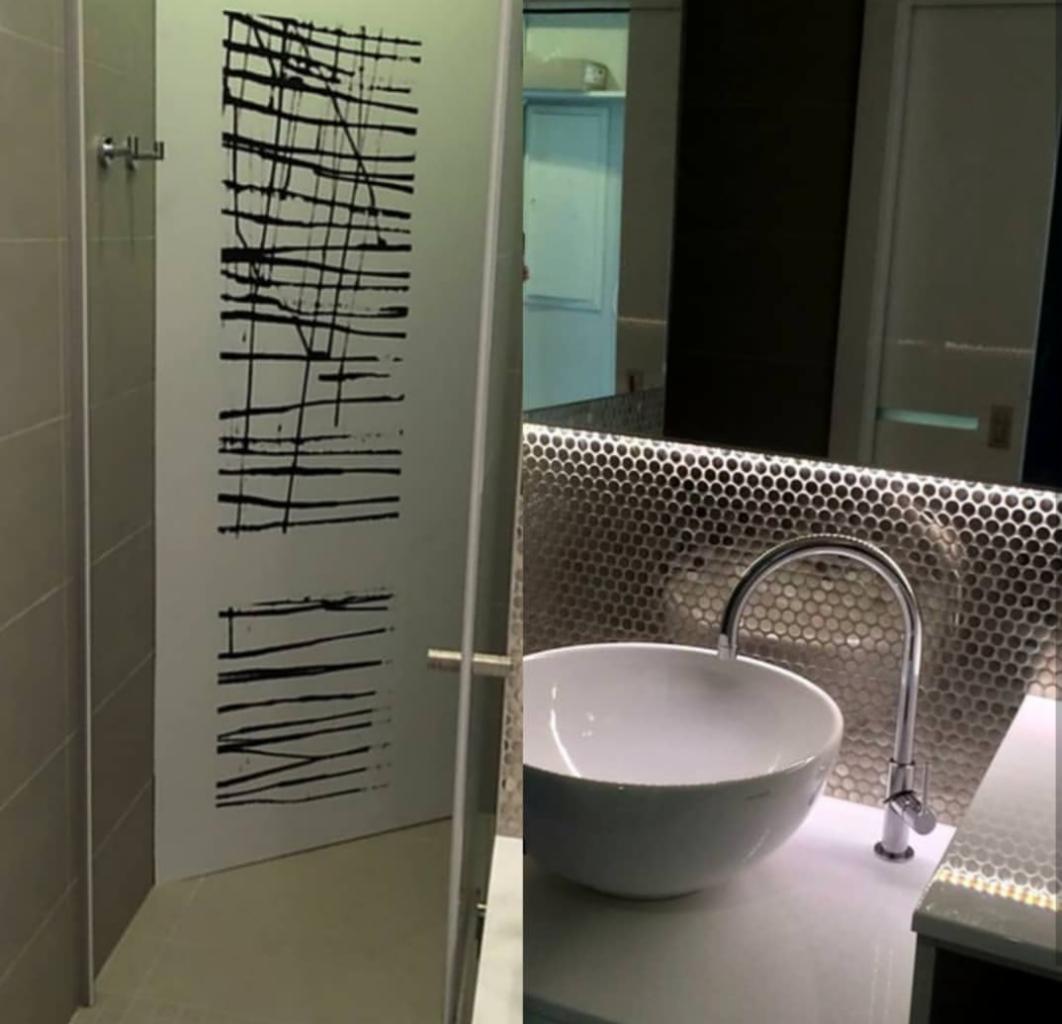 Nowoczesna łazienka z umywalką nablatową, baterią w kształcie łuku i metaliczną mozaiką na ścianie, z widoczną kabiną prysznicową z dekoracyjną grafiką na szkle.