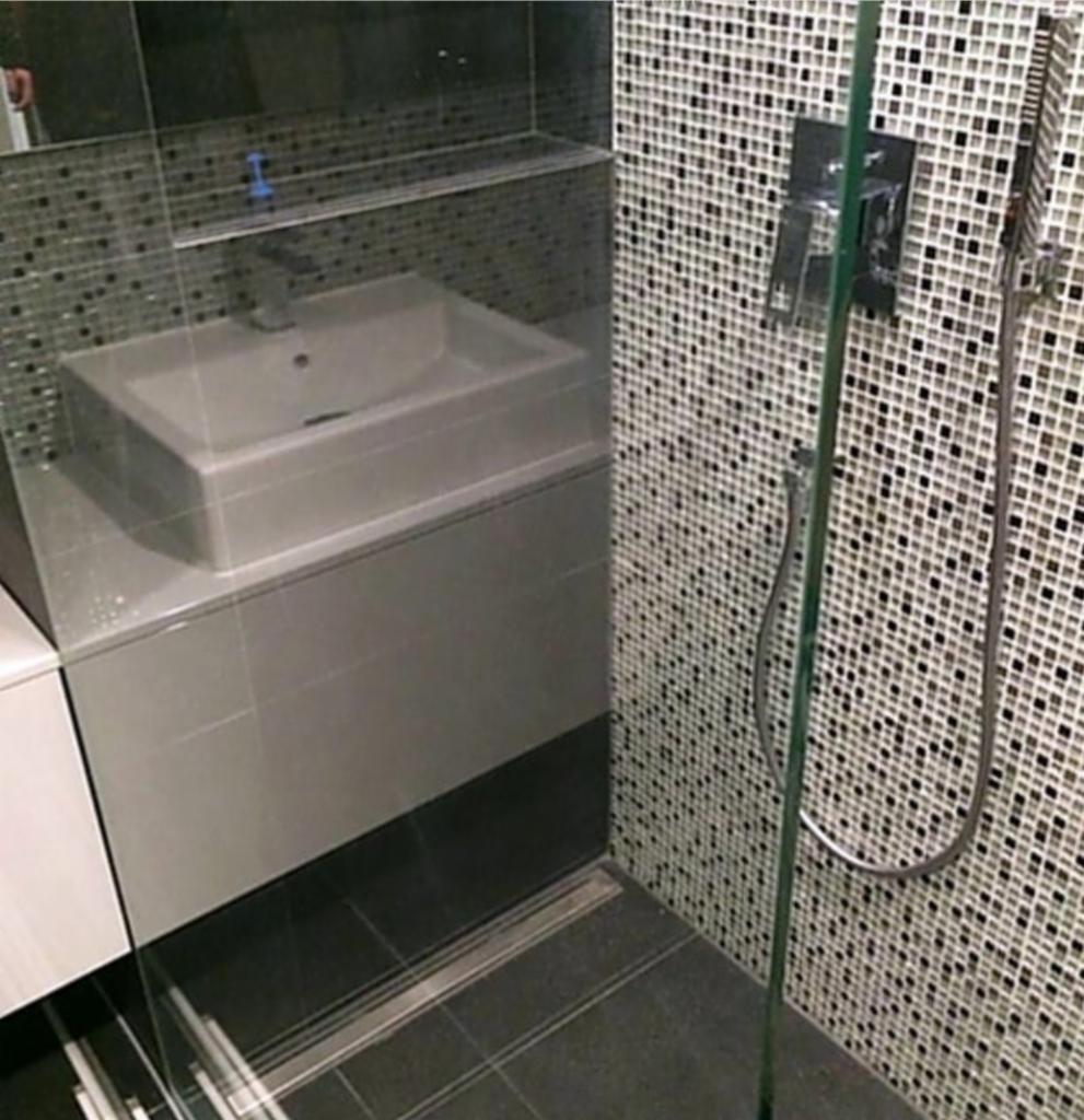 Umywalka nablatowa na szarej szafce w nowoczesnej łazience z mozaikową ścianą prysznicową i szklaną kabiną.