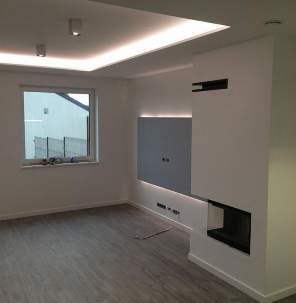 Nowoczesny salon z szarą podłogą imitującą drewno, białe ściany z podświetlanym panelem TV i minimalistycznym kominkiem, oświetlenie sufitowe LED.