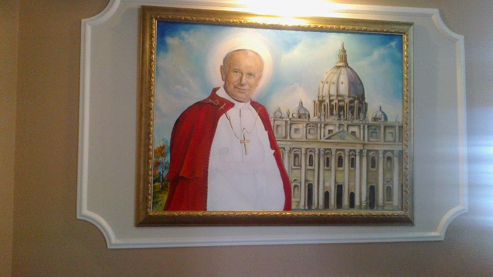 Obraz olejny przedstawiający Jana Pawła II na tle Bazyliki Świętego Piotra, w złotej ramie, powieszony w Lubaszowej na ścianie z dekoracyjną sztukaterią.