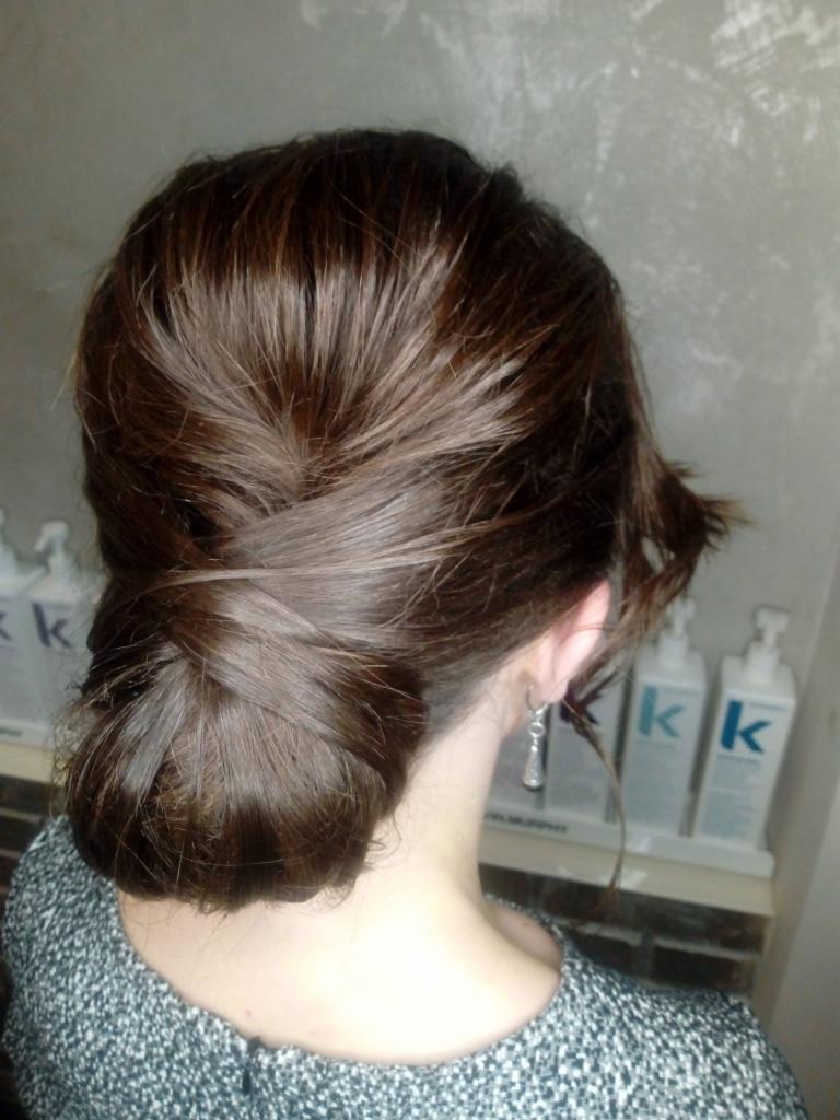 Upięcie włosów w kok z tyłu głowy, widoczne srebrne kolczyki i butelki kosmetyków do włosów w tle.