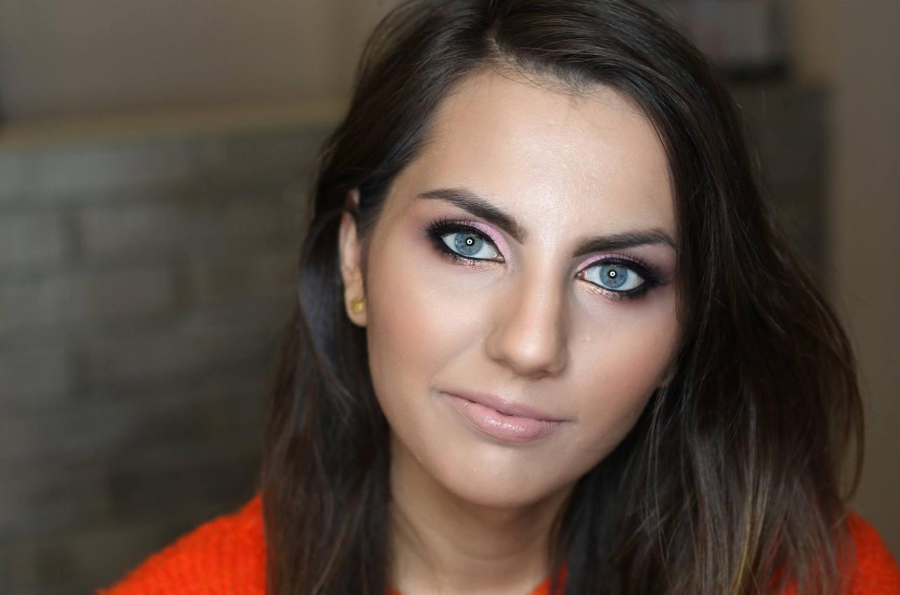 Portret kobiety z profesjonalnym makijażem oczu w odcieniach różu i czerni, podkreślającym intensywny błękit tęczówek; widoczna delikatna pomadka w kolorze nude i złote kolczyki.