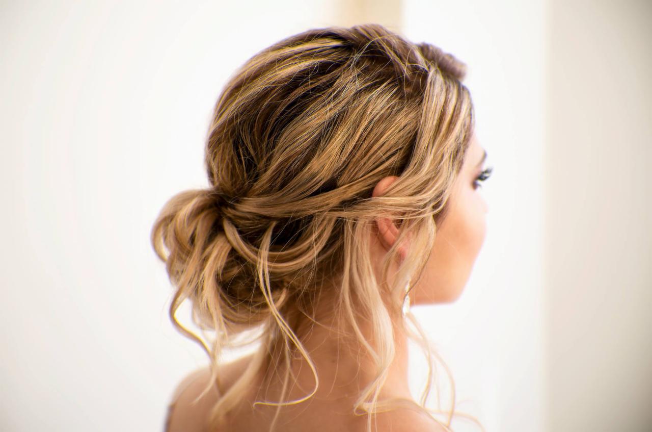 Upięcie włosów blond z pasemkami, widok z tyłu, delikatny kok z wypuszczonymi pasmami, elegancka fryzura na jasnym tle.