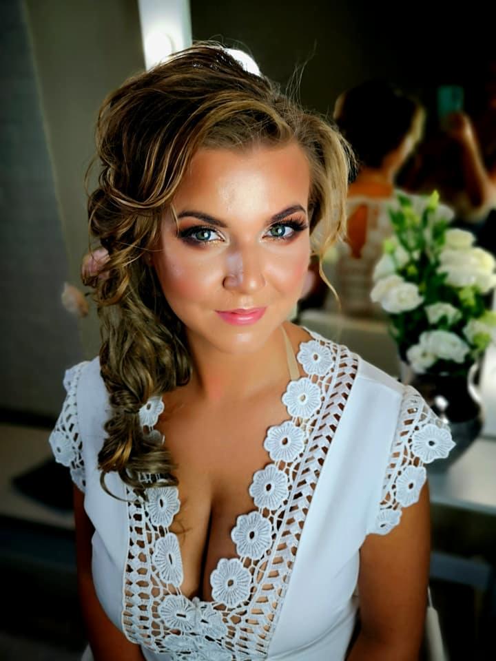 Portret kobiety z upiętymi włosami w stylu vintage i profesjonalnym makijażem, ubrana w białą sukienkę z koronkowym wykończeniem dekoltu.