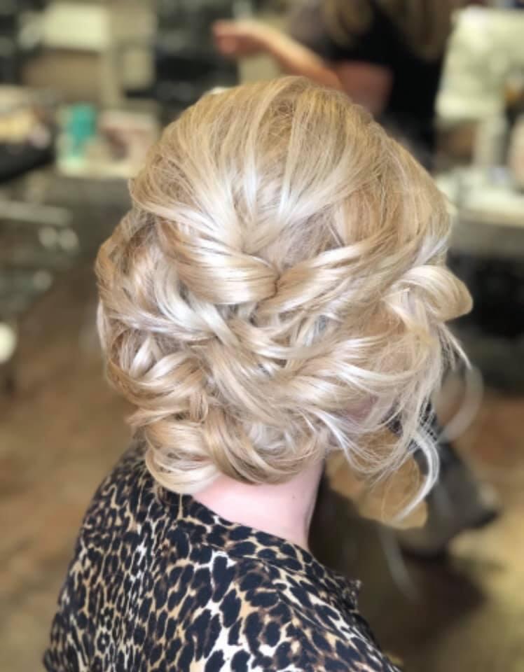 Upięcie blond włosów z tyłu głowy, z widocznymi skręconymi pasmami i delikatnymi refleksami, na tle rozmytego wnętrza salonu.