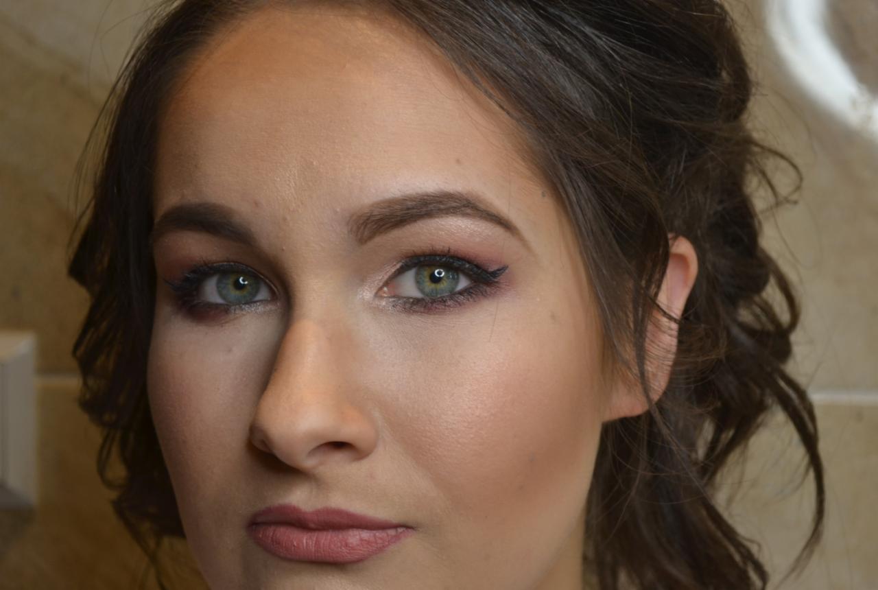 Portret kobiety z makijażem oczu w odcieniach różu i brązu, podkreślone zielone oczy, delikatny makijaż ust, upięte ciemne włosy.