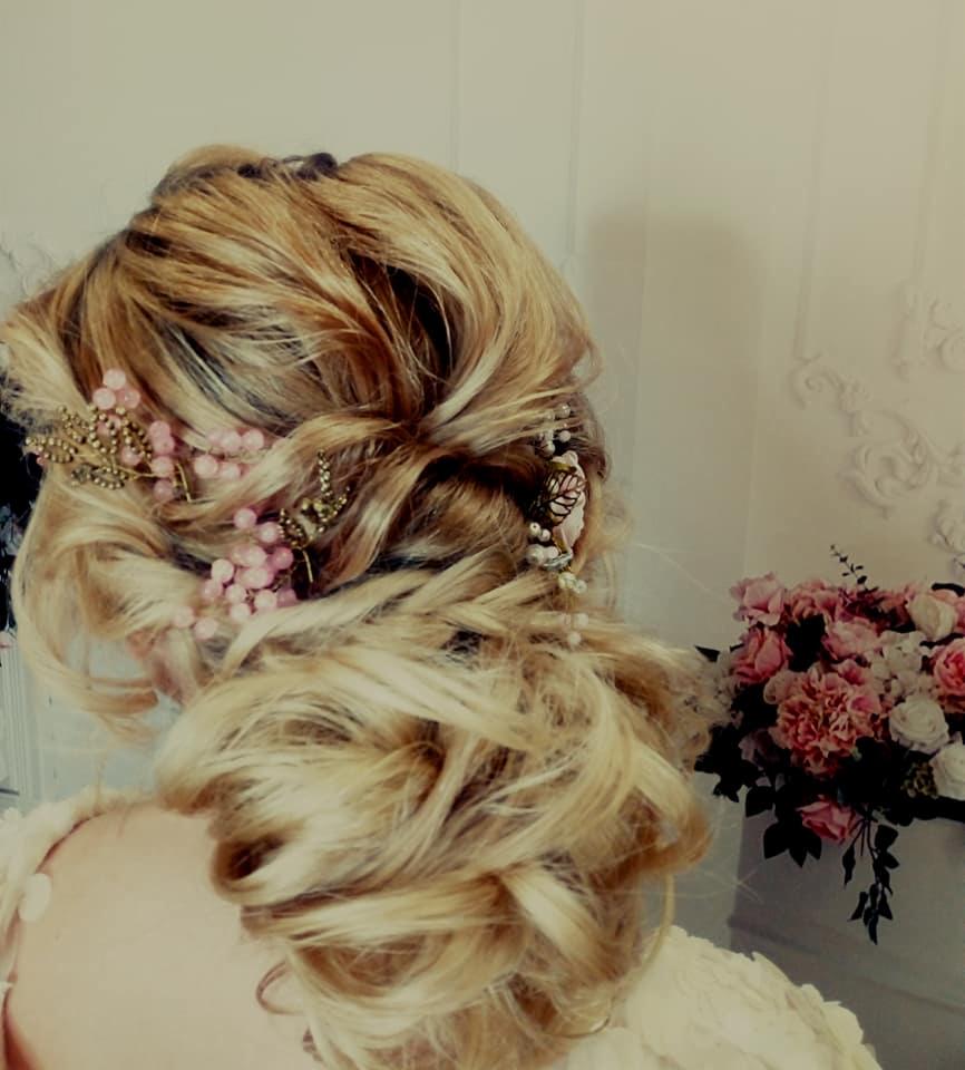 Upięcie blond włosów z ozdobami w postaci różowych koralików i złotych gałązek, widok z tyłu, obok bukiet różowych i białych kwiatów.
