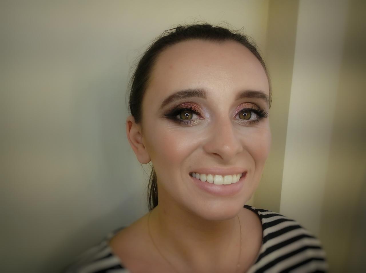 Uśmiechnięta kobieta z makijażem oczu w odcieniach brązu i różu, z widocznymi sztucznymi rzęsami i delikatnym makijażem twarzy.