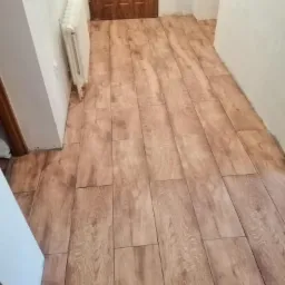 Ułożona podłoga z płytek imitujących drewno w korytarzu w Górze, widoczny grzejnik i fragment drzwi.