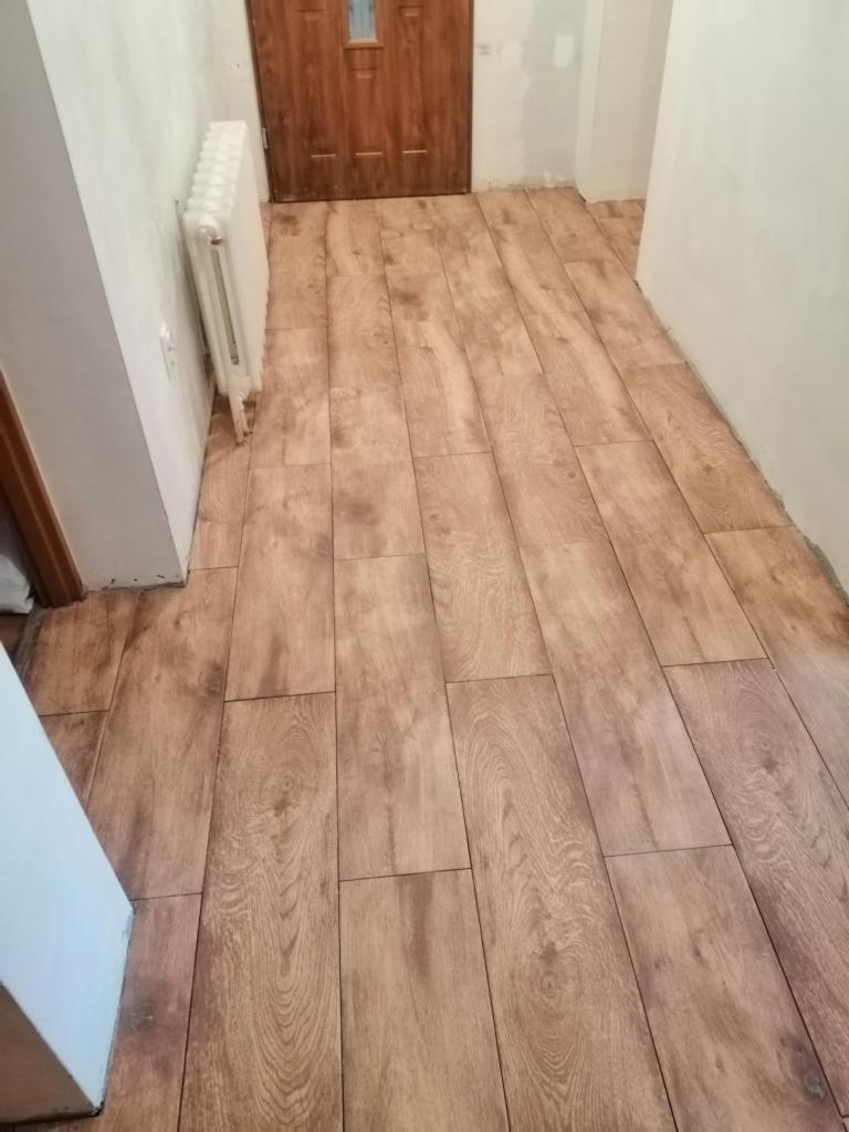 Ułożona podłoga z płytek imitujących drewno w korytarzu w Górze, widoczny grzejnik i fragment drzwi.