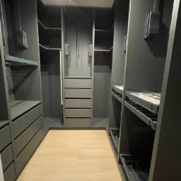 Nowoczesna garderoba w odcieniach szarości z drewnianą podłogą, oświetlona punktowymi lampami sufitowymi, z wysuwanymi półkami i szufladami.