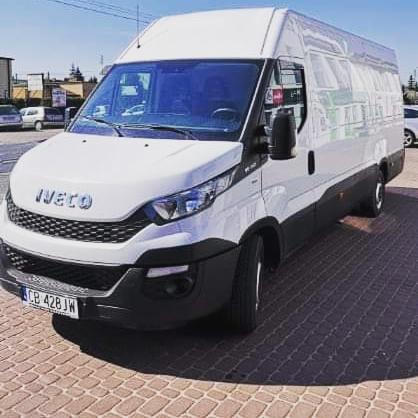 Biały bus marki Iveco na kostce brukowej, widok z przodu i boku, tablica rejestracyjna CB 428JW, w tle budynki i drzewa.