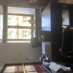 Gabinet z biurkiem, krzesłami i widokiem na budynek z dekoracyjną fasadą za oknem z żaluzjami.