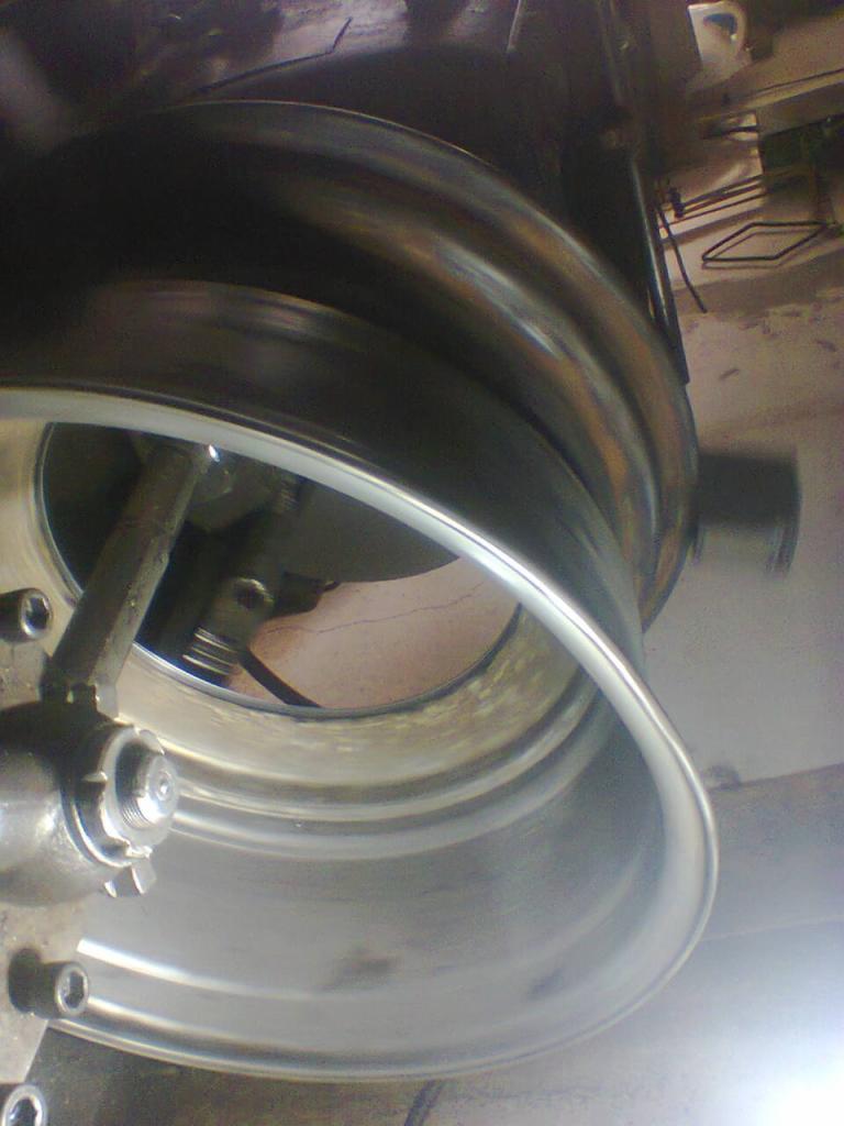 Metalowa obręcz koła zamocowana w uchwycie tokarskim podczas obróbki, widoczne ślady użytkowania i niedoskonałości powierzchni.