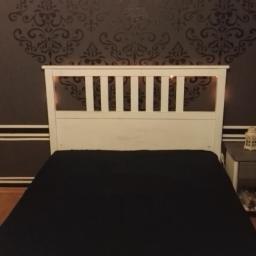 Kamil Spólnik - Ciemna ściana w sypialni z ornamentowym wzorem w odcieniach szarości, biała rama łóżka z czarną narzutą, nocna lampka na stoliku.