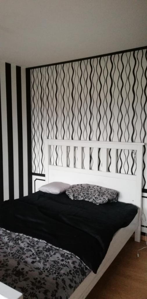 Sypialnia z białą ramą łóżka, czarną pościelą i wzorzystą tapetą w czarno-białe pasy oraz fale.