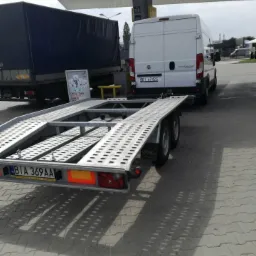 Laweta z podłączonym białym busem na stacji benzynowej, w tle widoczna naczepa ciężarówki z plandeką.