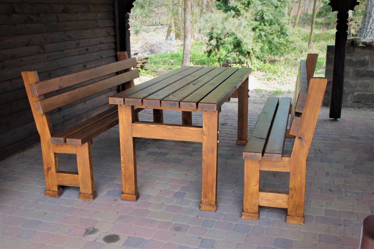 Rustykalny zestaw mebli ogrodowych z drewna w Chełmnie: stół i dwie ławki z wysokimi oparciami, całość w ciepłym, brązowym odcieniu, ustawione na brukowanym patio.