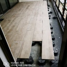 Montaż podłogi z płytek imitujących drewno na balkonie, widoczne regulowane wsporniki pod płytami, częściowo ułożone płytki.