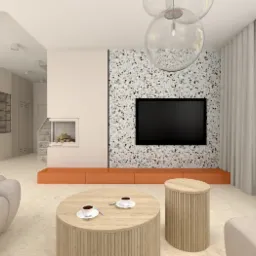 Jasne, przestronne wnętrze salonu z telewizorem na ścianie z mozaiką, okrągłym drewnianym stolikiem kawowym z dwiema filiżankami, kominkiem i nowoczesną sofą w neutralnych barwach.