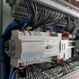 Szczegółowe ujęcie rozdzielnicy elektrycznej z licznymi przewodami podłączonymi do listew zaciskowych i modułu zasilania, widoczne oznaczenia na urządzeniach.