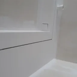 Świeżo pomalowane na biało wnętrze łazienki z zabudową kartonowo-gipsową, widoczny otwór rewizyjny, rura kanalizacyjna i gniazdko elektryczne.