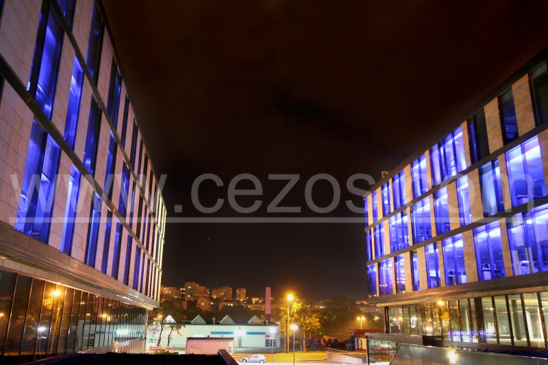 Nocny widok na budynek biurowy w Gdyni z niebieskim oświetleniem elewacji, widoczne miasto w tle i lampy uliczne.