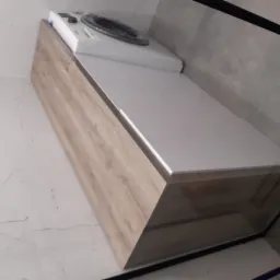 Zabudowa pralki z drewnopodobną okleiną i białym blatem w łazience z marmurowymi płytkami.