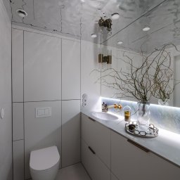 TOMASZ KRALKA FIRMA HANDLOWO USŁUGOWA STOLMAX - Nowoczesna łazienka z białymi szafkami na wymiar, umywalką i toaletą. Lustro z podświetleniem i dekoracyjnym wazonem. Sufit z efektem lustrzanym.