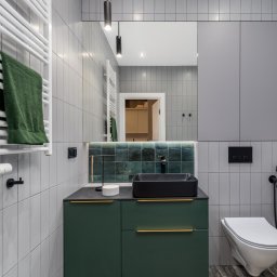 TOMASZ KRALKA FIRMA HANDLOWO USŁUGOWA STOLMAX - Nowoczesna łazienka z zieloną szafką pod umywalką i szarą zabudową w Iwanowicach Włościańskich. Minimalistyczny design, płytki w odcieniach szarości i złote akcenty.