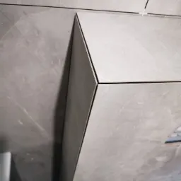 Szare, matowe płytki imitujące marmur, ułożone z precyzją na ścianie i obudowie. Widoczne fugi w kolorze czarnym i biały krzyżyk dystansowy. Minimalistyczny design.