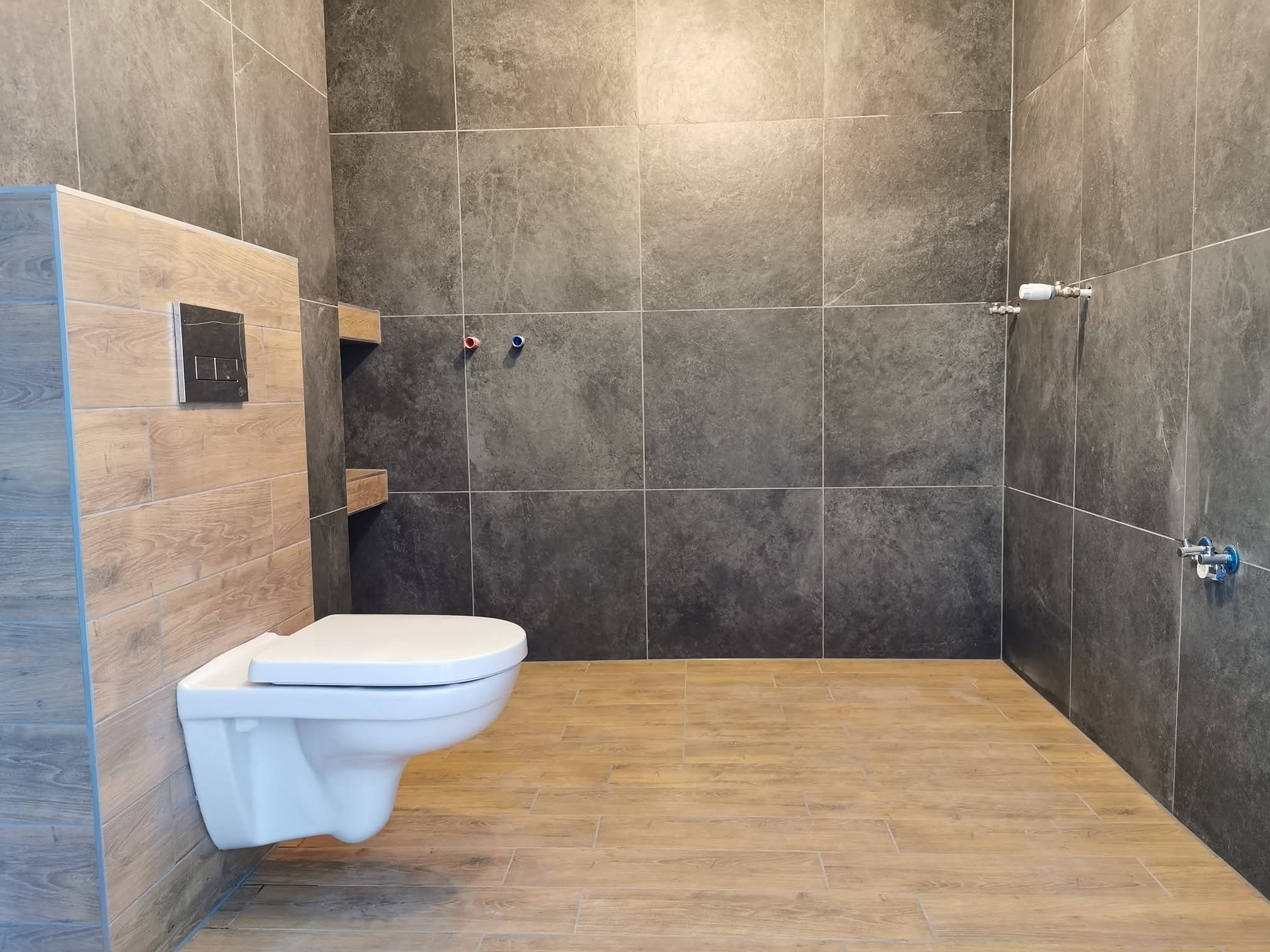 Nowoczesna łazienka w Jaszkowej Dolnej z podwieszaną toaletą i szarą, kamienną okładziną ścienną, imitującą drewno. Minimalistyczne wykończenie i armatura.