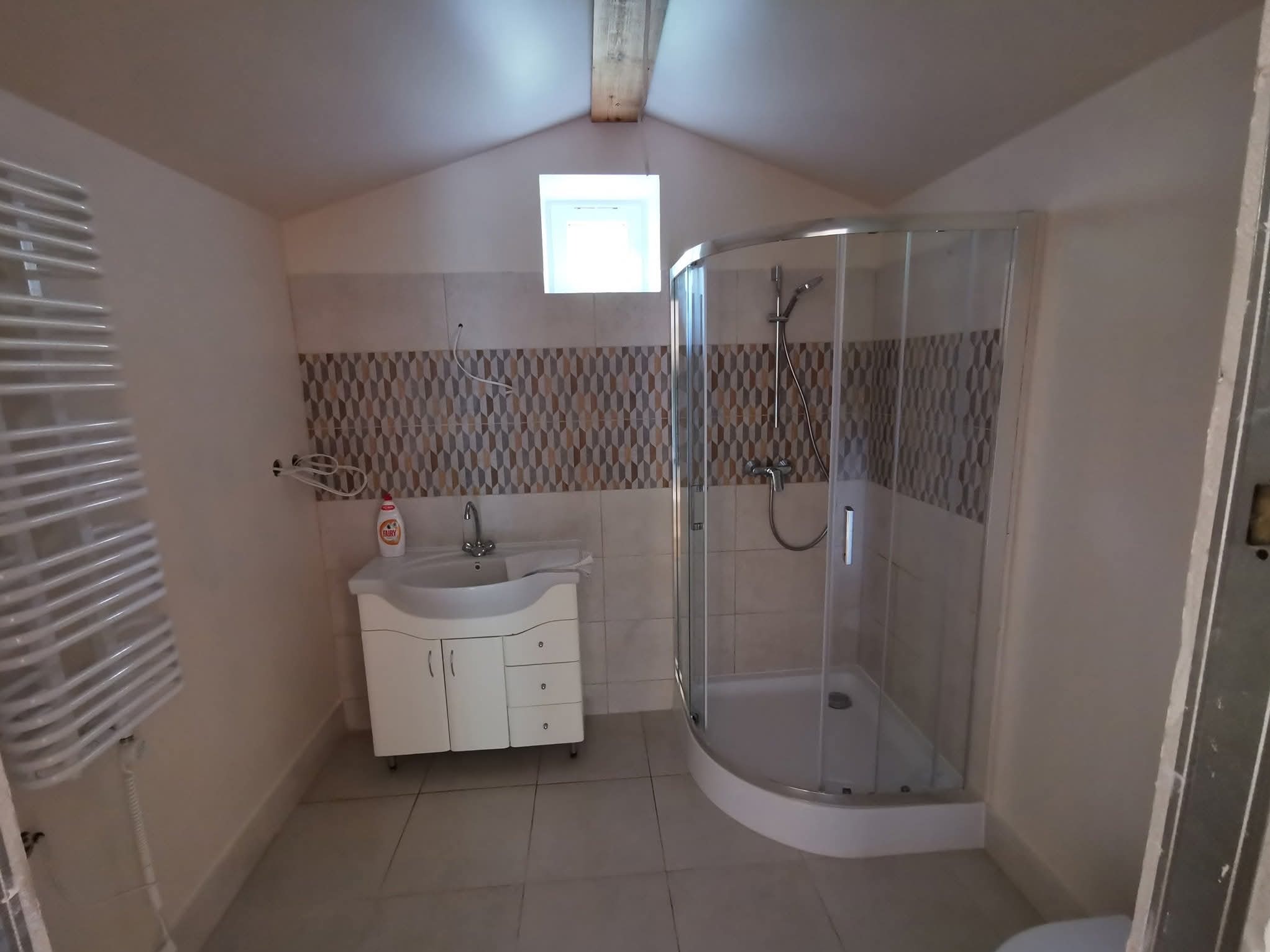 Wykończona łazienka na poddaszu ze skośnym sufitem. Kabina prysznicowa z brodzikiem, umywalka z szafką i grzejnik drabinkowy.