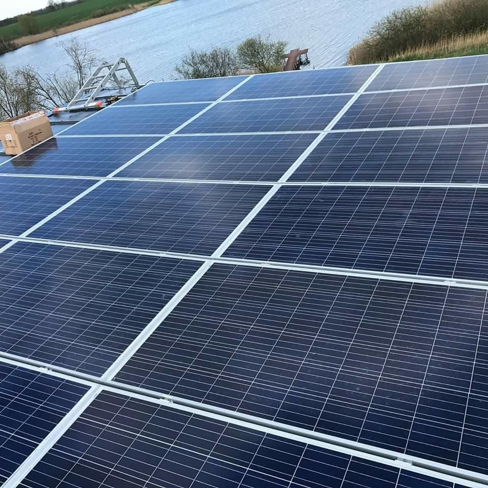 Widok z góry na zainstalowane panele słoneczne na dachu budynku, z jeziorem i zielenią w tle, obok leży karton po panelach.