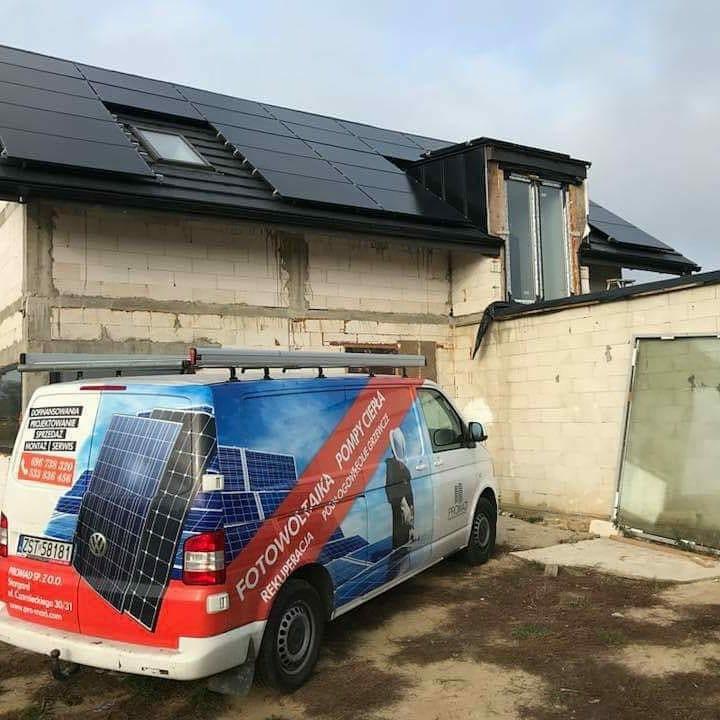 Dom w trakcie wykończenia z panelami słonecznymi na dachu, obok zaparkowany van z reklamą firmy instalującej systemy odnawialnych źródeł energii.