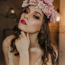 Portret kobiety z błyszczącym cieniem do powiek w odcieniach różu i fuksjową szminką, noszącej wianek z różowych kwiatów i sukienkę z koronkowymi zdobieniami.