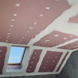 Marcin Włodarczyk - Montaż płyt kartonowo-gipsowych na poddaszu z oknem dachowym, widoczne szpachlowane łączenia i punkty mocowania, surowe ściany w tle.