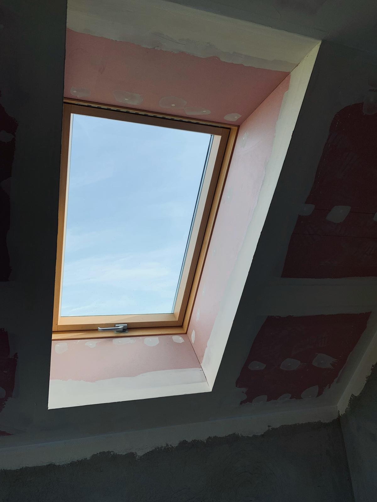 Montaż okna dachowego w konstrukcji z surowymi ścianami, widoczne łączenia płyt przygotowane do szpachlowania.