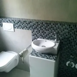 Nowoczesna łazienka z wiszącą toaletą, umywalką nablatową na szafce i mozaiką w odcieniach szarości na ścianach.