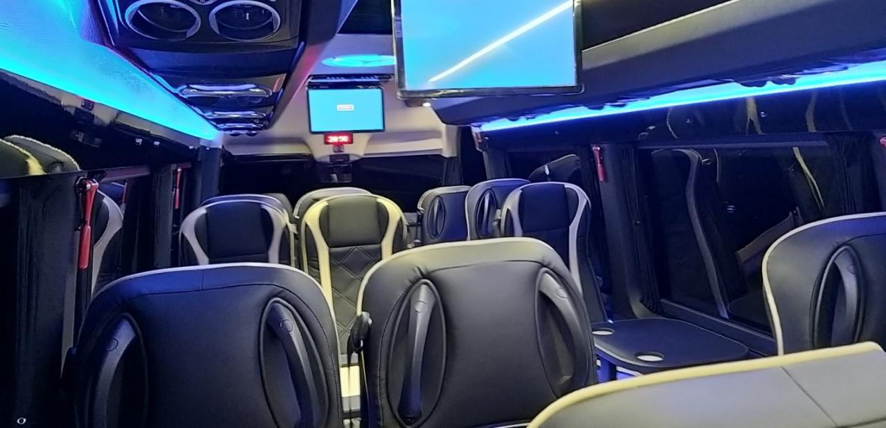 Wnętrze luksusowego busa z czarnymi skórzanymi fotelami, podświetleniem LED i zamontowanymi ekranami LCD.