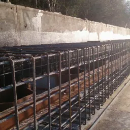 Siatka zbrojeniowa ułożona wzdłuż wykopu, przygotowana do zalania betonem, widoczne drewniane elementy szalunku i betonowa ściana w tle.