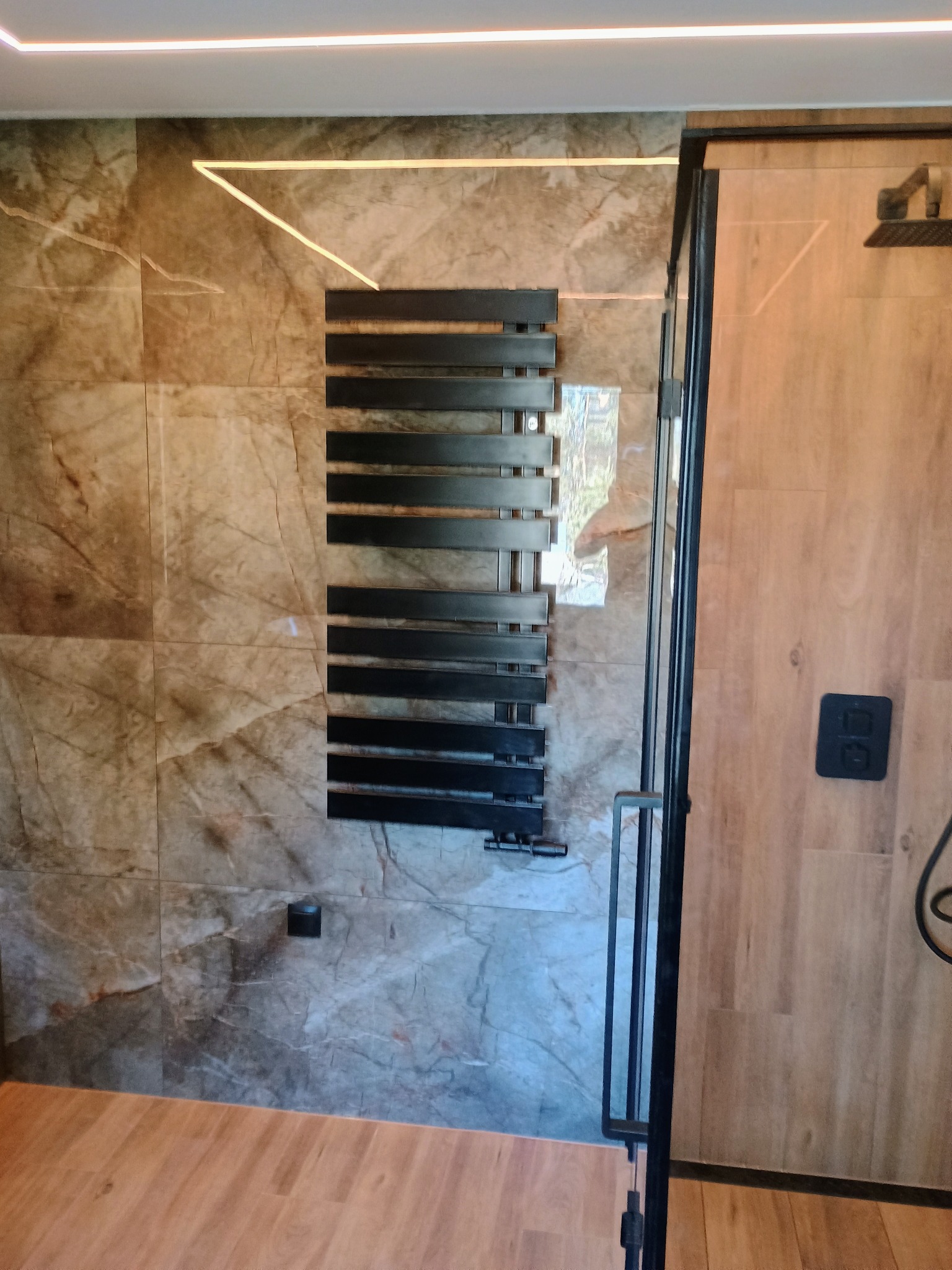 Nowoczesna łazienka w Kluczach z marmurowymi płytkami, czarnym grzejnikiem drabinkowym i szklaną kabiną prysznicową z drewnopodobnymi panelami.