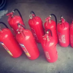 Grupa ustawionych, czerwonych gaśnic proszkowych z czarnymi wężami na szarym podłożu.