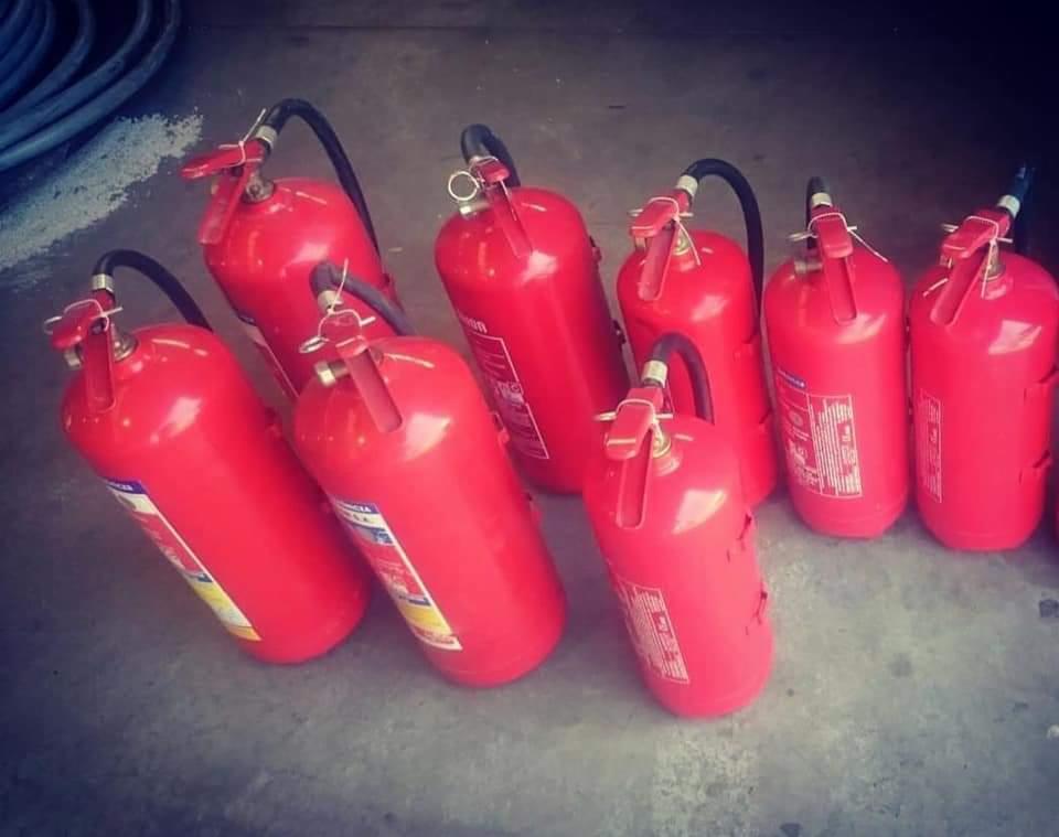 Grupa ustawionych, czerwonych gaśnic proszkowych z czarnymi wężami na szarym podłożu.