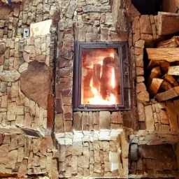 Kamienny kominek z paleniskiem i ułożonym obok drewnem opałowym, dekoracja ze słomy i kwiatów na ścianie