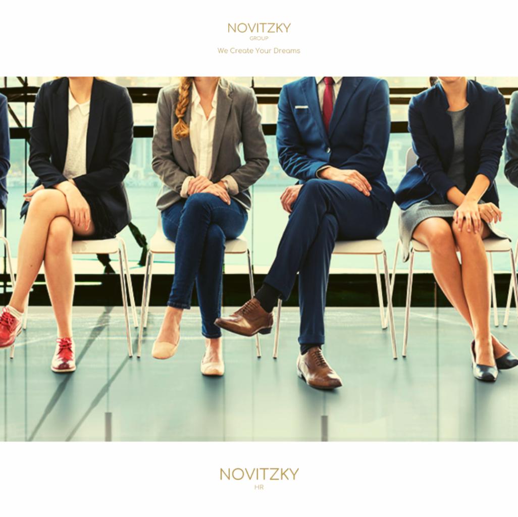 Osoby w strojach biznesowych siedzą na krzesłach, czekając na rozmowę kwalifikacyjną, z widokiem na miasto w tle.