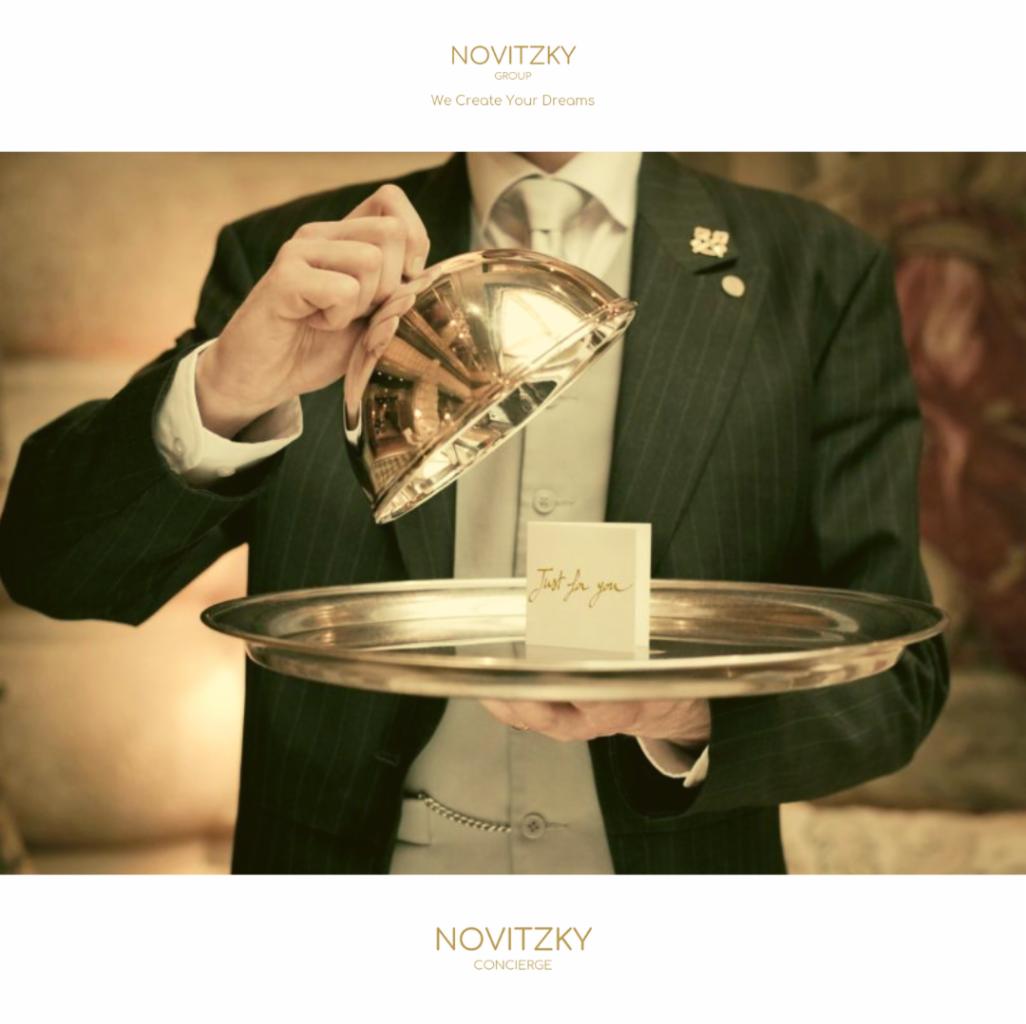 Elegancki kelner w liberii unosi srebrną pokrywę nad tacą z kartką 'Just for you', prezentacja usługi concierge.