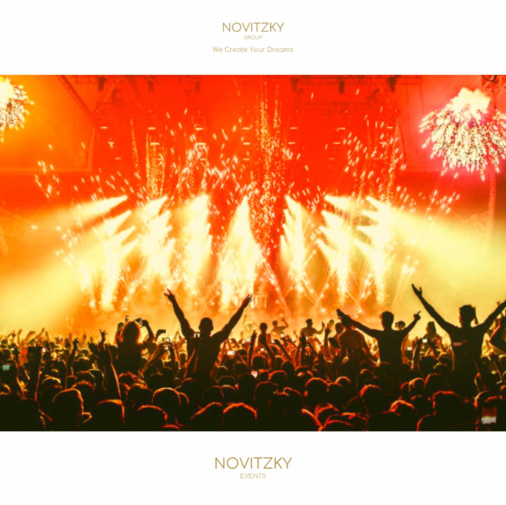 Tłum ludzi z podniesionymi rękami podczas pokazu fajerwerków na koncercie, oświetlenie sceniczne w odcieniach pomarańczy i żółci.