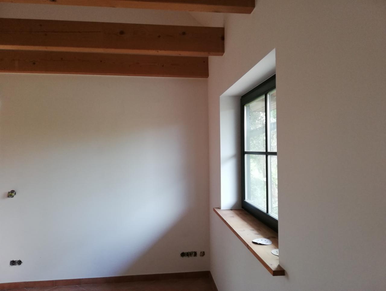 Wnętrze pokoju po odświeżeniu ścian, widoczne drewniane belki stropowe, okno z drewnianym parapetem i przygotowane do montażu gniazdka elektryczne.